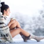 woman drinking coffee wearing knitted nordic print poncho sitting home by the window